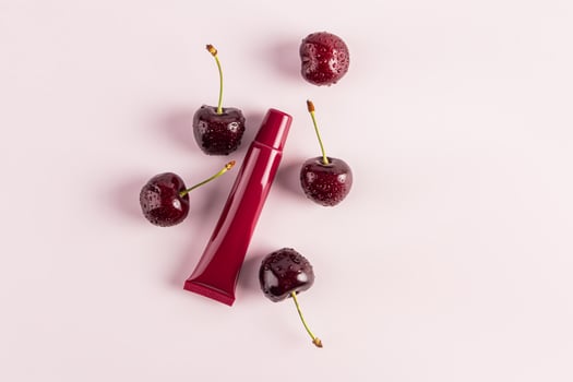 burgundy beauty tube with mask, balm, lip gloss on a pink background among spell cherries. top view. Blank packaging layout. product advertising. photo