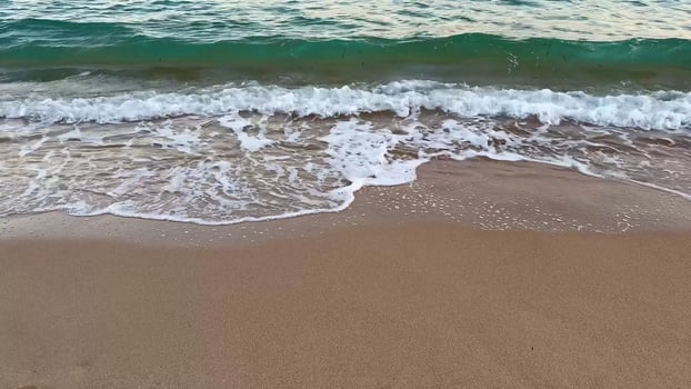 A beautiful beach scene characterized by gentle waves lapping against the warm sand, with a distant shoreline at sunset photo