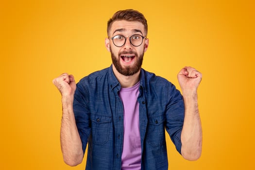 Winner and success concept. Excited young guy making YES gesture with clenched fists on orange studio background. Excited Caucasian man shouting OMG, overjoyed with big win photo