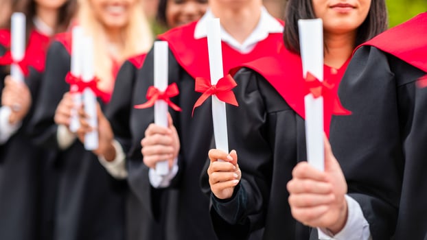 Unrecognizable international group of male and female graduators wearing graduation robes showing their diplomas, closeup. High school, university college graduation concept photo