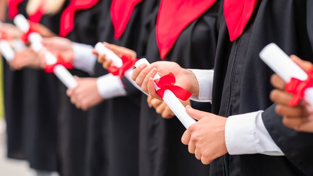 Hands of unrecognizable multiethnic group of male and female graduators wearing graduation robes showing their diploma scrolls. High school, university college graduation concept photo