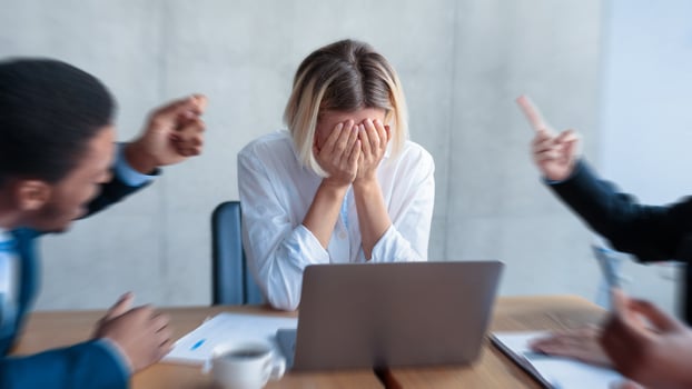 Victimization At Workplace. Colleagues Shouting At Unhappy Victimized Businesswoman, While She Covering Face With Hands Sitting In Modern Office. Corporate Communication Problem And Adult Bullying photo