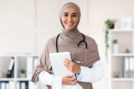 Modern technologies in healthcare concept. Happy female doctor in hijab posing with digital tablet in her office, copy space. Muslim woman therapist holding digital pad, clinic interior photo