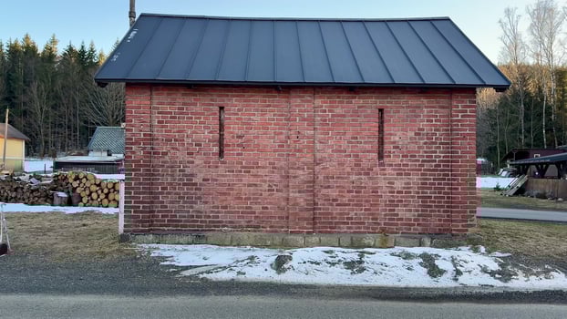 A rustic brick building with a weathered roof, surrounded by fresh snow and tall trees in a tranquil winter scene photo