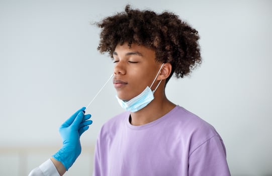 Coronavirus diagnostics. Doctor in rubber gloves making nasal coronavirus PCR test for African American teen, using sterile swab stick indoors. Black adolescent undergoing covid-19 testing procedure photo