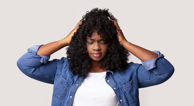 Upset young black lady in jeans coat and white t-shirt with curly hair having headache, touching her head, closing eyes, grey studio background. Migraine, headache, tension, cluster concept photo