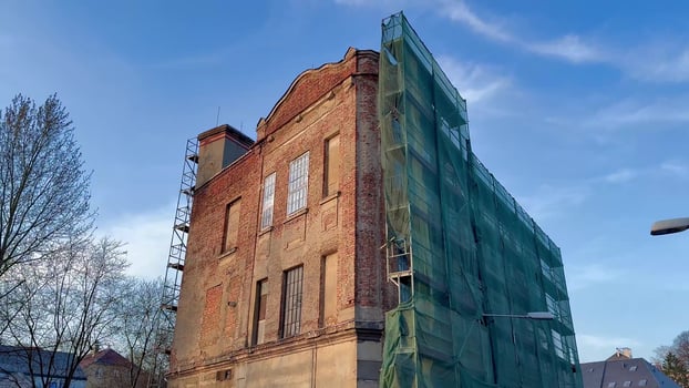 A historic brick building undergoing renovation, covered with green scaffolding, showcasing construction work. photo