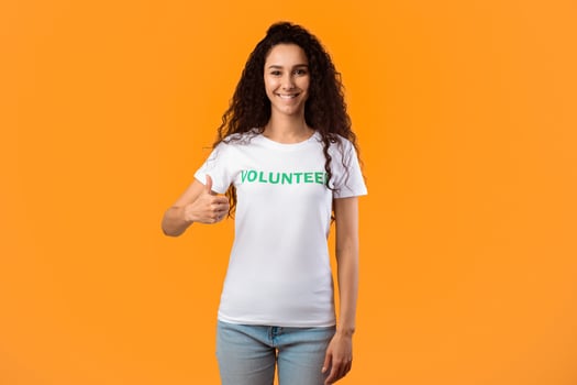 I Like Volunteering. Cheerful Volunteer Lady Gesturing Thumbs Up Smiling To Camera Standing Over Yellow Studio Background. Female Activist Showing Thumbs-Up Approving Something photo