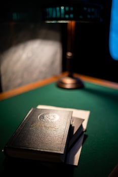 Vintage Leather-Bound Books Stacked on a Green Felt Table Beside a Classic Lamp Casting Warm Light in a Cozy Study photo
