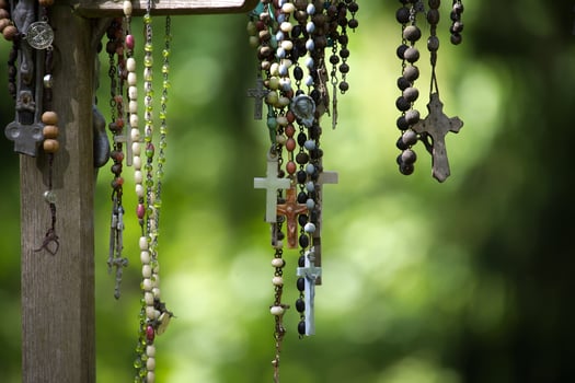 Various rosaries with crosses and beads hang against a soft, green backdrop. photo