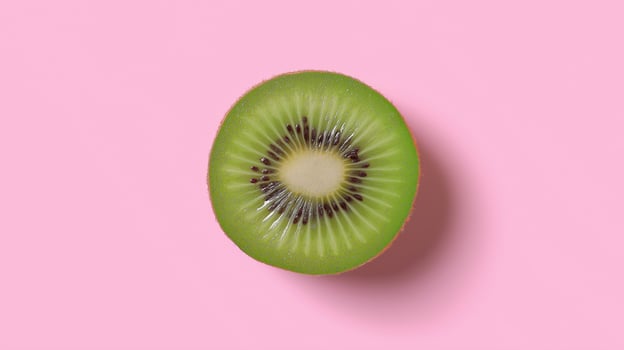 Bright green kiwi slice reveals seeds and texture against a pastel pink backdrop. photo