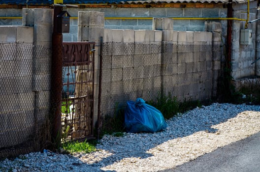 A blue plastic bag is sitting on the ground next to a gate. The gate is rusted and the bag is placed on the ground in front of it photo