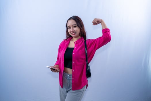 Asian Indonesian woman wearing red dress carrying black bag smiling and raising one hand photo