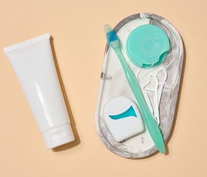 Set of oral hygiene items, tube of toothpaste, toothbrush, dental floss placed on small oval tray, on beige background. Top view photo