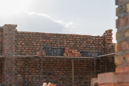 Construction progress shows brick wall rising with scaffolding support under bright sky in an urban setting photo