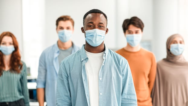 New Reality And Epidemic Concept. Diverse group of international people wearing protective medical masks, standing indoors, posing and looking at camera. Selective focus on african american man photo