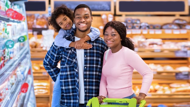 Portrait of happy black family posing together at grocery store. African American parents with cute daughter looking at camera and smiling at shopping mall. Satisfied customers at supermarket photo
