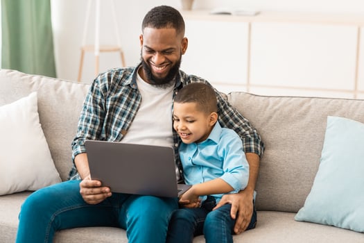 African Daddy Embracing Little Son Sitting With Laptop Watching Cartoons Online On Computer Spending Time Together And Bonding At Home. Weekend With Loving Dad. Father's Day Concept photo
