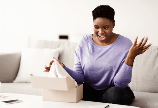 Wrong Package. Portrait of surprised frustrated black woman unpacking box, shocked by bad delivery service sitting on sofa at home in living room. Lady confused by shipping mistake, copy space photo