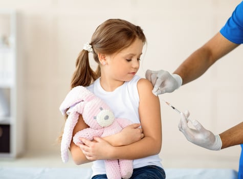 Doctor doing injection of coronavirus vaccine to little girl with toy bunny at clinic. Cute child on visit to medical specialist, getting immunization against coronavirus. Medicine and vaccination photo