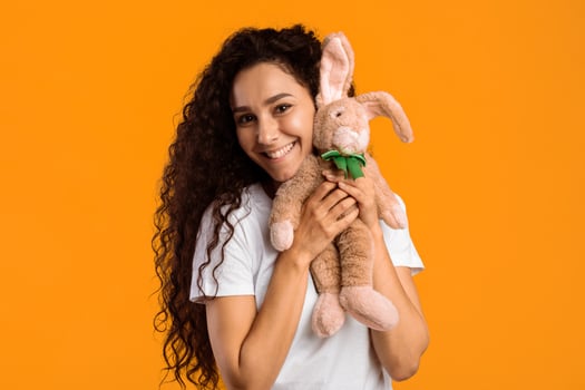 Volunteer Woman Holding Bunny Toy Smiling To Camera Standing Over Yellow Background. Studio Shot. Charity Aid For Kids, Volunteering And Animals Protection Concept photo