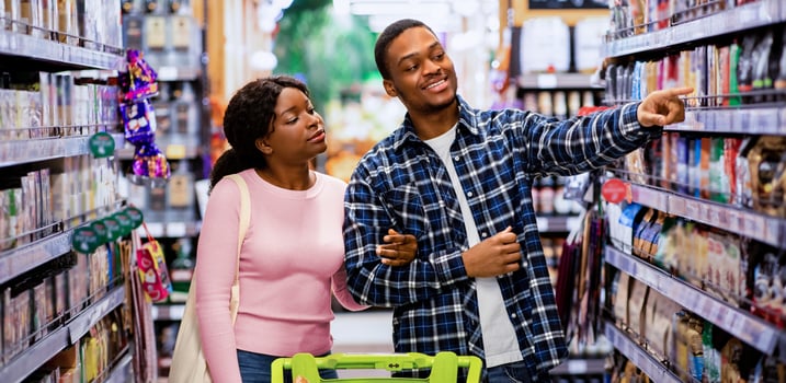 Pretty black woman and her boyfriend shopping for groceries together, selecting goods, pointing at shelves in supermarket. Loving African American couple choosing food at produce section of big mall photo