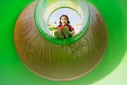Joyful Child Playing in Colorful Playground Slide Captured from Inside Viewpoint with Bright Green Surroundings, Fun Outdoor Activity Daytime photo