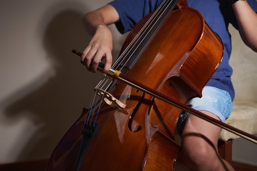 An image capturing the hands of a cellist gripping a bow and playing a cello. The lighting highlights the instrument's polished wood, symbolizing musical passion and creativity. photo