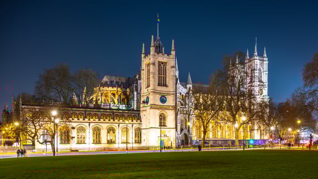 Illuminated Westminster Abbey stands tall against the night sky in London. Surrounding trees and lamp posts frame the majestic structure, showcasing its architectural beauty. photo