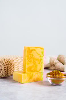 Bars of homemade turmeric soap and powder in bowl on table vertical view photo