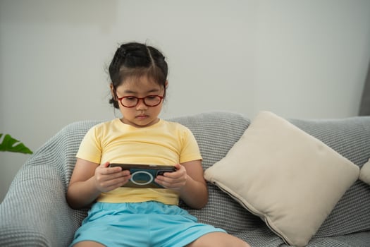 Focused Young Girl Engaged in Interactive Game on Smartphone While Sitting Comfortably on Soft Couch Surrounded by Bright Indoor Space photo