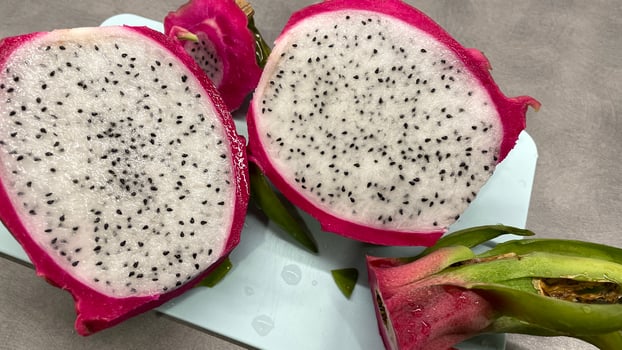 Large red dragonfruit cut in half, lying on a blue cutting board photo