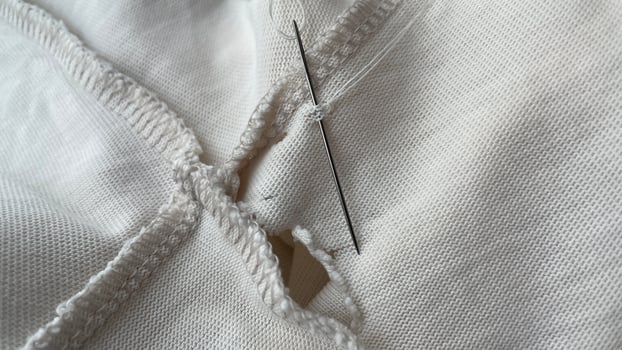 needle and thread sewing holes in beige waxed fabric, close-up, seams and texture, torn old clothes photo