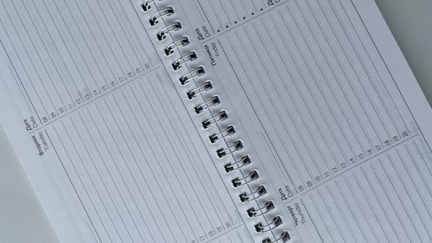 Minimalist close-up of an open spiral-bound weekly planner featuring days of the week in both Russian and English. Perfect for illustrating organization, productivity, and time management in international or bilingual settings. Ideal for business, educati photo