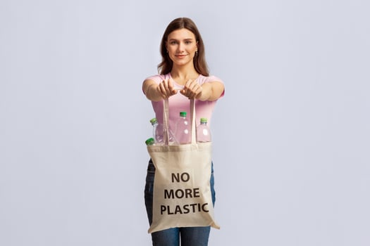 No More Plastic. Happy Young Lady Carrying Eco Tote Bag With Empty Bottles For Recycling, Smiling Nature-Lover Woman Promoting Zero-Waste Living, Posing Over Light Studio Background, Copy Space photo