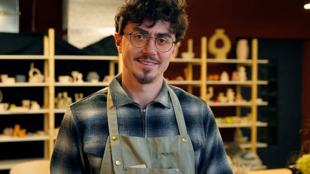 A man in glasses and an apron stands in front of a shelf photo