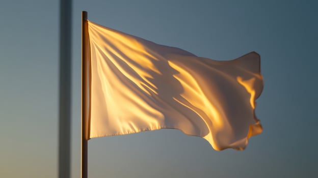 A white flag flutters in the soft glow of the setting sun. The gentle breeze suggests movement, as the fabric catches the light beautifully. The background features a serene sky photo