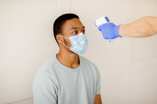 Doctor or nurse using infrared thermometer to measure temperature of black male patient before covid-19 vaccination at clinic. Medical healthcare and coronavirus immunization concept photo