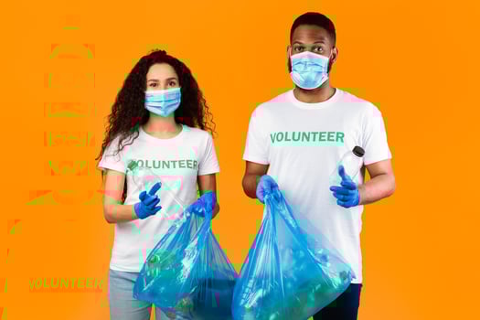 Two Multiethnic Volunteers Holding Plastic Bottles And Blue Garbage Bags With Litter Standing On Yellow Studio Background. Waste Sorting And Plastic Disposal. Keep Planet Clean Concept photo