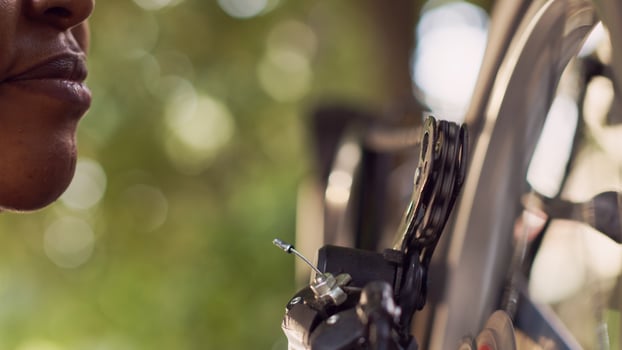Sports-loving black woman cautiously greasing and maintaining her bike disc brake ring outside. Close-up view of female carefully lubricating rusty bicycle with specialized chain lubricant. photo