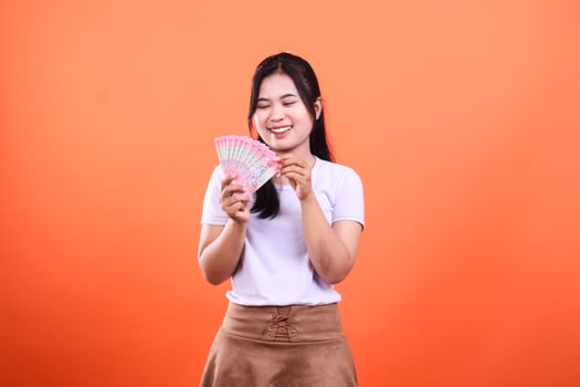 Woman holding fanned banknotes against an orange backdrop in a studio setting photo