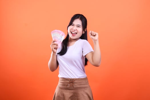 Excited woman holds fan of pink Indonesian rupiah notes on orange background photo