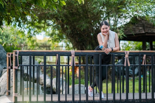 A young woman leans on a wooden bridge in a serene garden, surrounded by greenery and rocks, enjoying a peaceful moment outdoors. photo