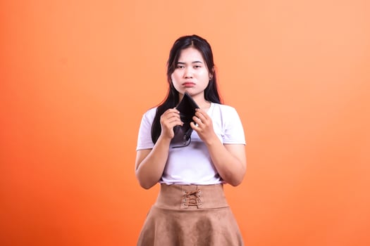 A woman holding an empty wallet looking disappointed on orange background photo