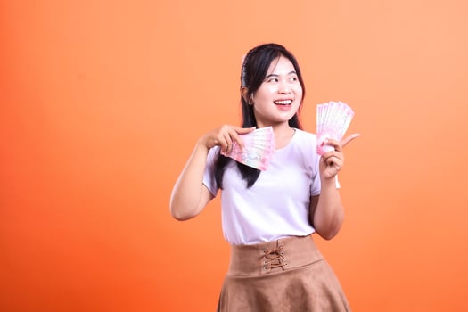 Excited woman holding Indonesian Rupiah banknotes against an orange background photo