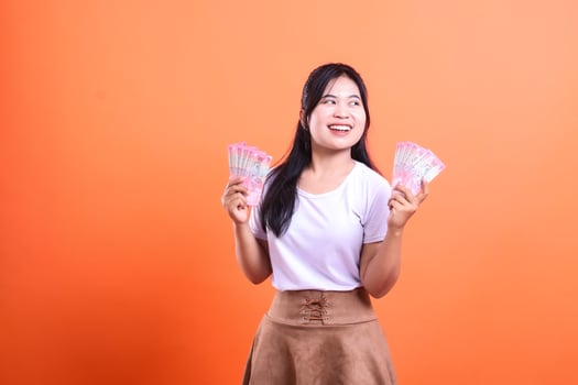 Woman holding money with a orange background, showing an expression of happiness photo