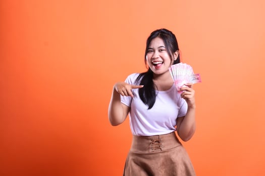 Excited woman pointing at rupiah money with an orange background and white shirt photo