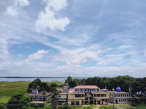 Peaceful semi urban landscape with buildings, lush trees, and a waterbody beneath cumulus clouds. Perfect for themes of rural beauty, heritage, and natural serenity. photo