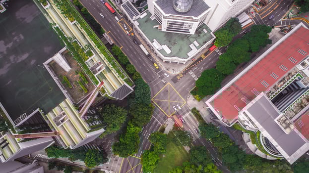 Aerial image of a Singapore intersection featuring a yellow box junction, modern buildings, a rooftop garden, trees, and vehicles like a red bus. photo