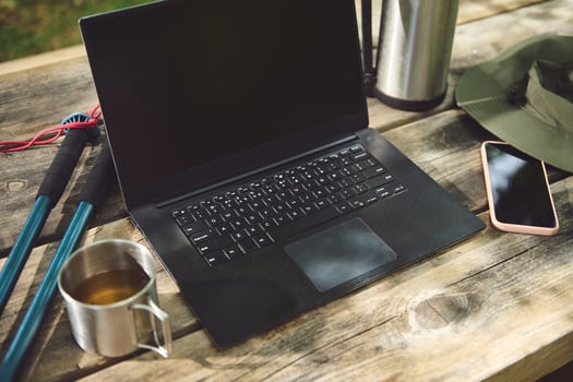 Outdoor Workspace Featuring a Laptop, Mobile Phone, and Accessories on a Wooden Table photo